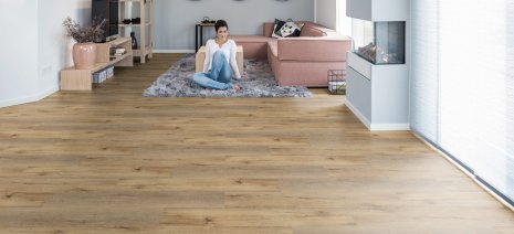 wineo Bodenbelag im Wohnzimmer mit Frau vorm Sofa und Teppich